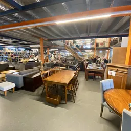 Winkelvloer met diverse meubelen en huishoudartikelen, waaronder houten tafels, stoelen, kasten en zitmeubels.