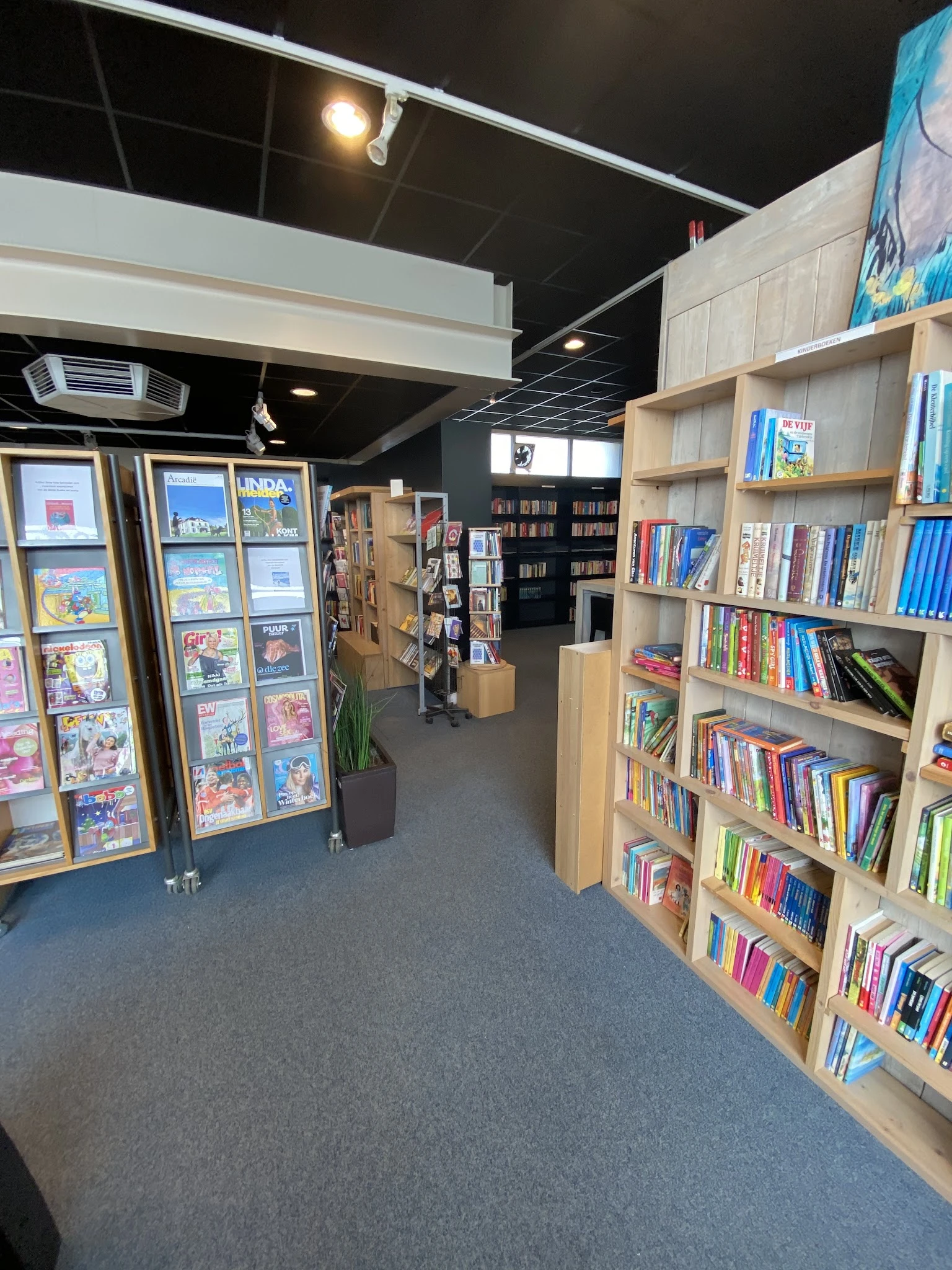 Winkelvloer met houten stellingen vol boeken, displays met stripboeken en een zwart plafond