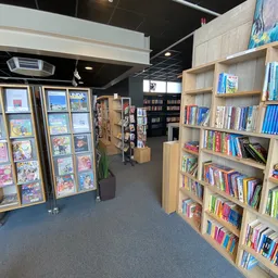 Winkelvloer met houten stellingen vol boeken, displays met stripboeken en een zwart plafond
