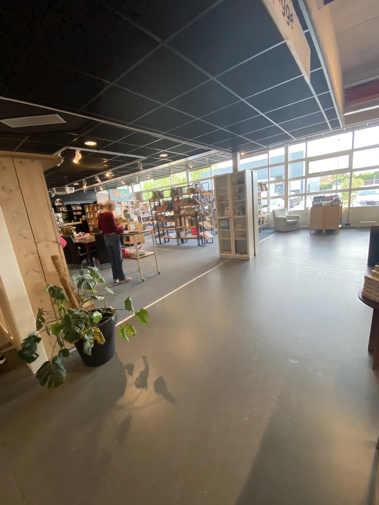 Winkelvloer van kringloopwinkel met boekenrekken, zithoeken en grote ramen aan voorkant
