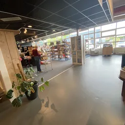 Winkelvloer van kringloopwinkel met boekenrekken, zithoeken en grote ramen aan voorkant