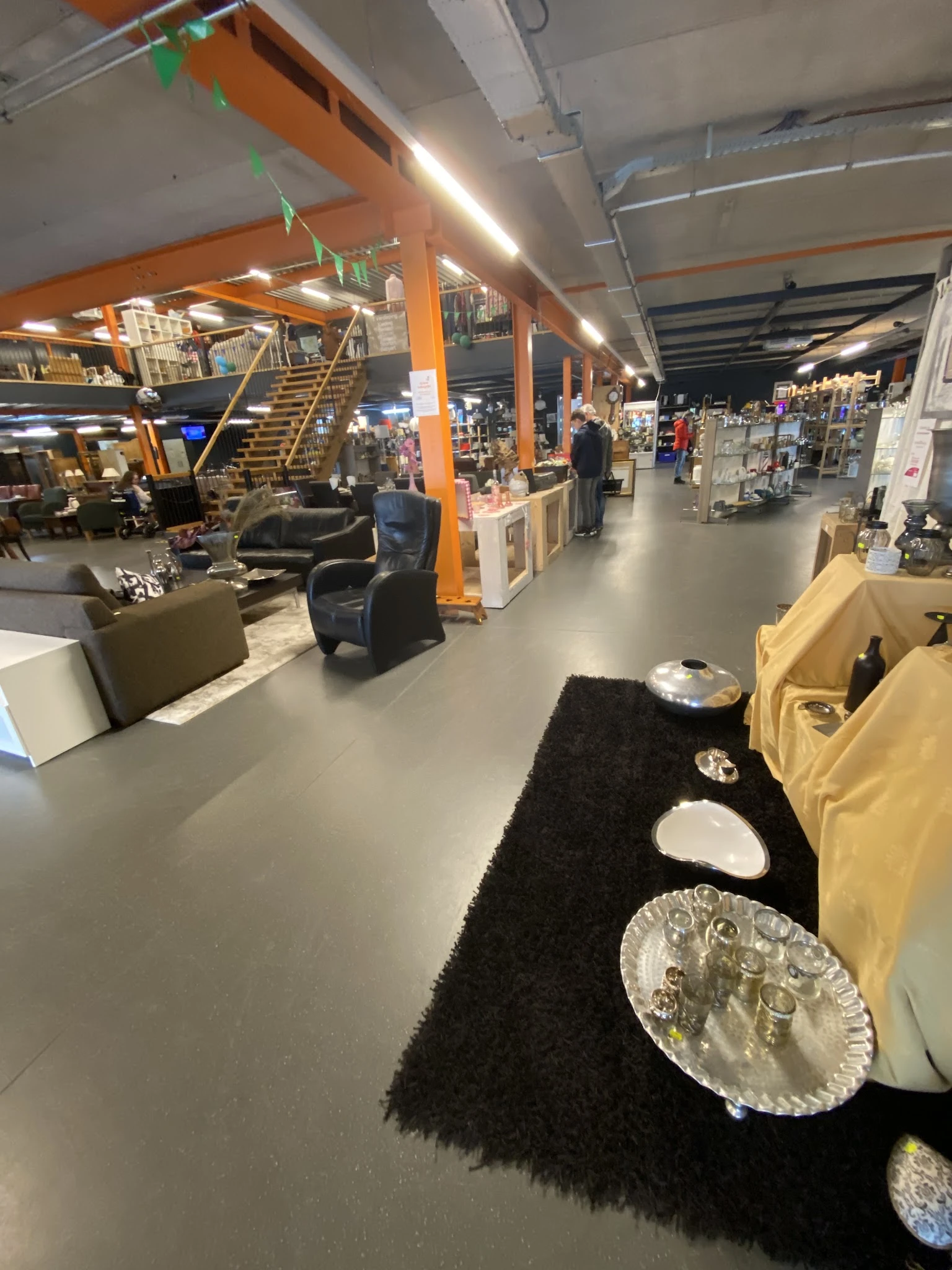 Ruim winkelbinnenland met diverse meubels, decoratie en huishoudartikelen uitgestald onder oranje kolommen