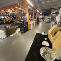 Ruim winkelbinnenland met diverse meubels, decoratie en huishoudartikelen uitgestald onder oranje kolommen