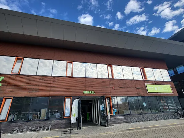 Voorgevel van kringloopwinkel met houten lambrisering, grote ramen en WINKEL-opschrift, onder blauwe hemel