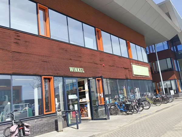 Gevel van kringloopwinkel met houten lambrisering, grote ramen en oranje details, met fietsen ervoor geparkeerd