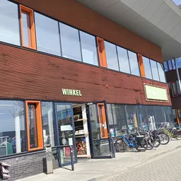Gevel van kringloopwinkel met houten lambrisering, grote ramen en oranje details, met fietsen ervoor geparkeerd