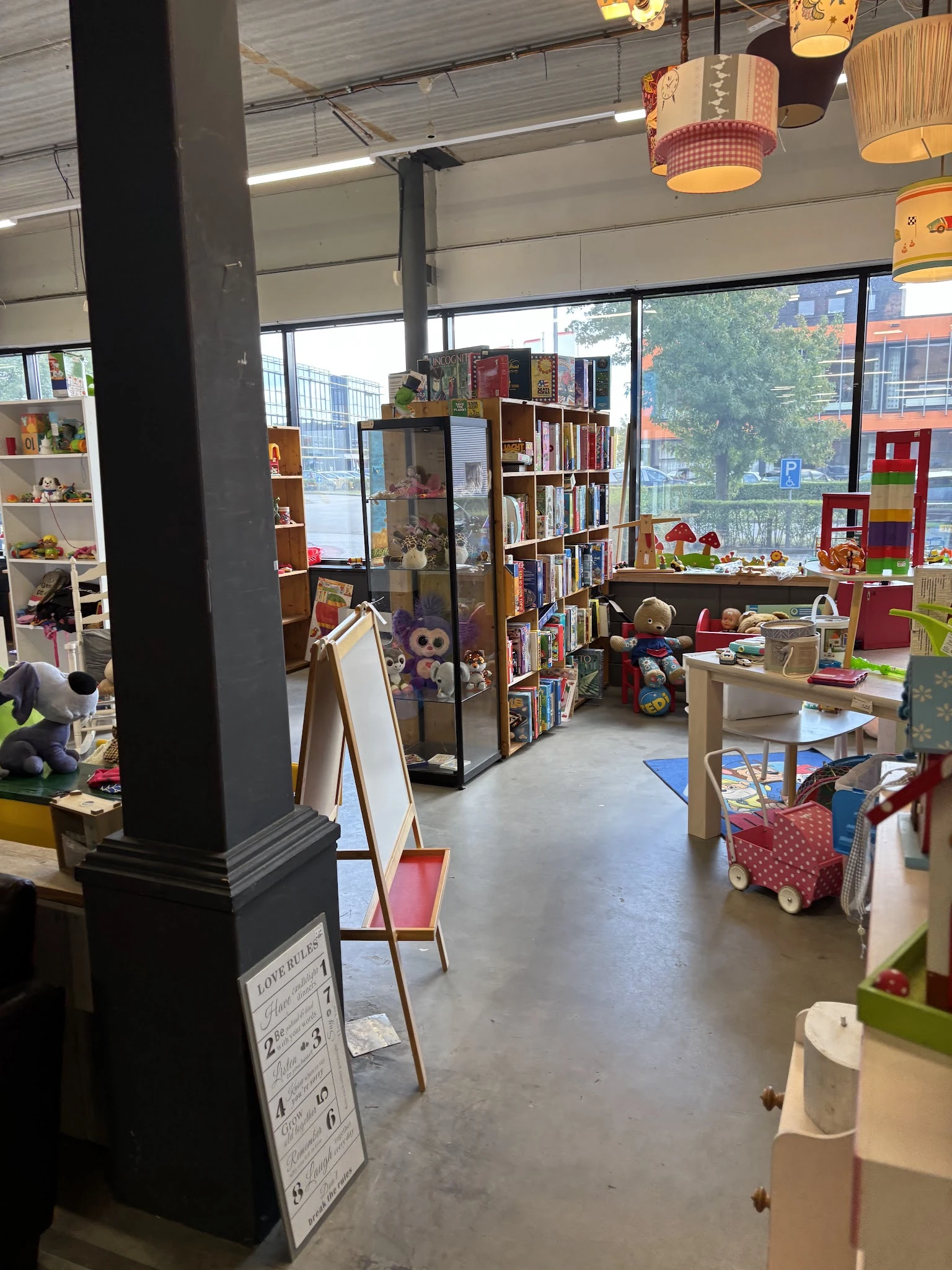 Speelhoek in kringloopwinkel met boeken, speelgoed, rode zitmeubels en houten speelgoed