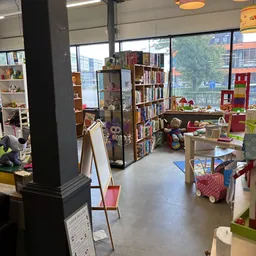 Speelhoek in kringloopwinkel met boeken, speelgoed, rode zitmeubels en houten speelgoed
