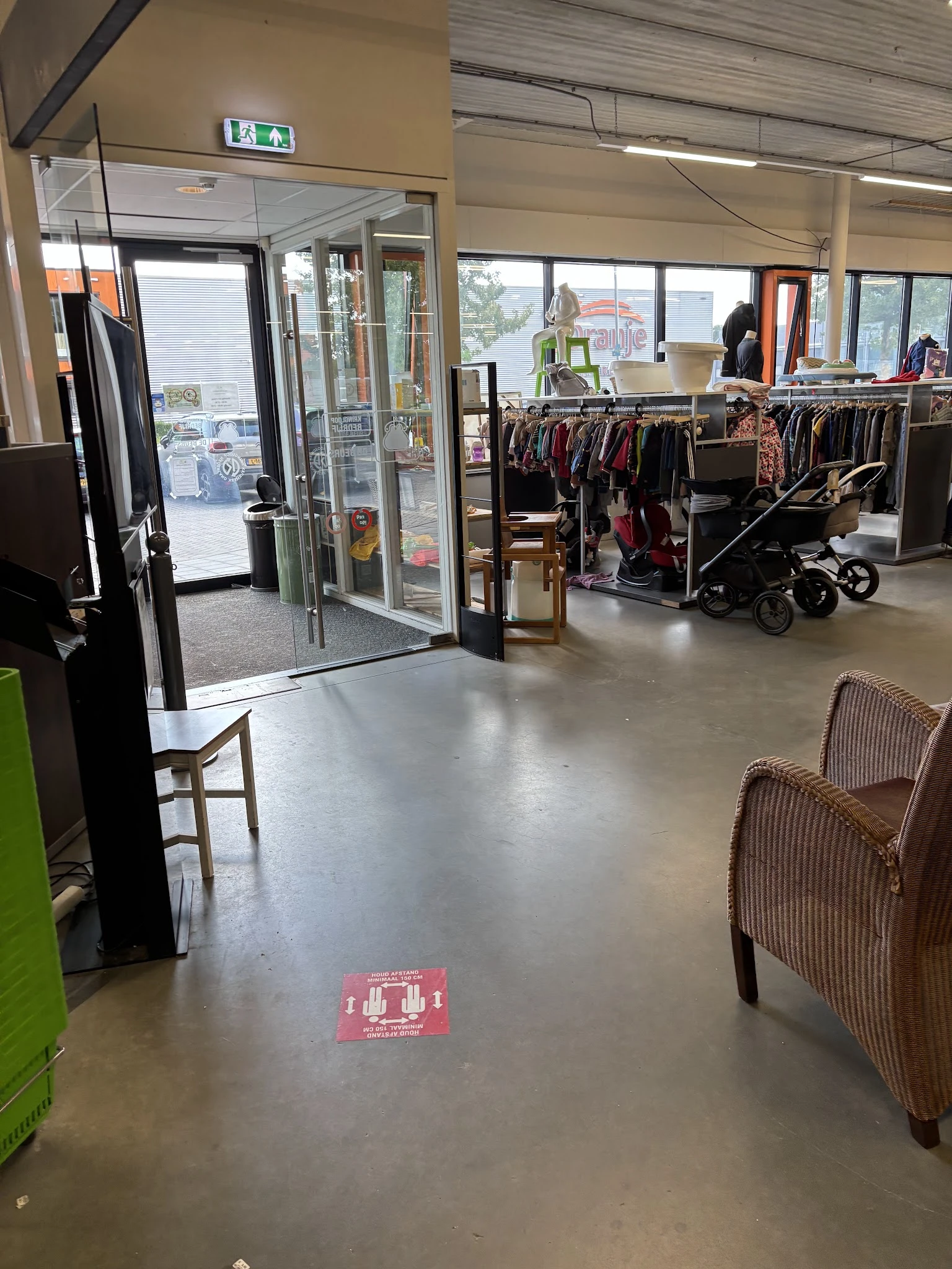 Winkelvloer van kringloopwinkel met kledingrekken, kinderwagen en enkele stoelen
