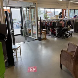 Winkelvloer van kringloopwinkel met kledingrekken, kinderwagen en enkele stoelen