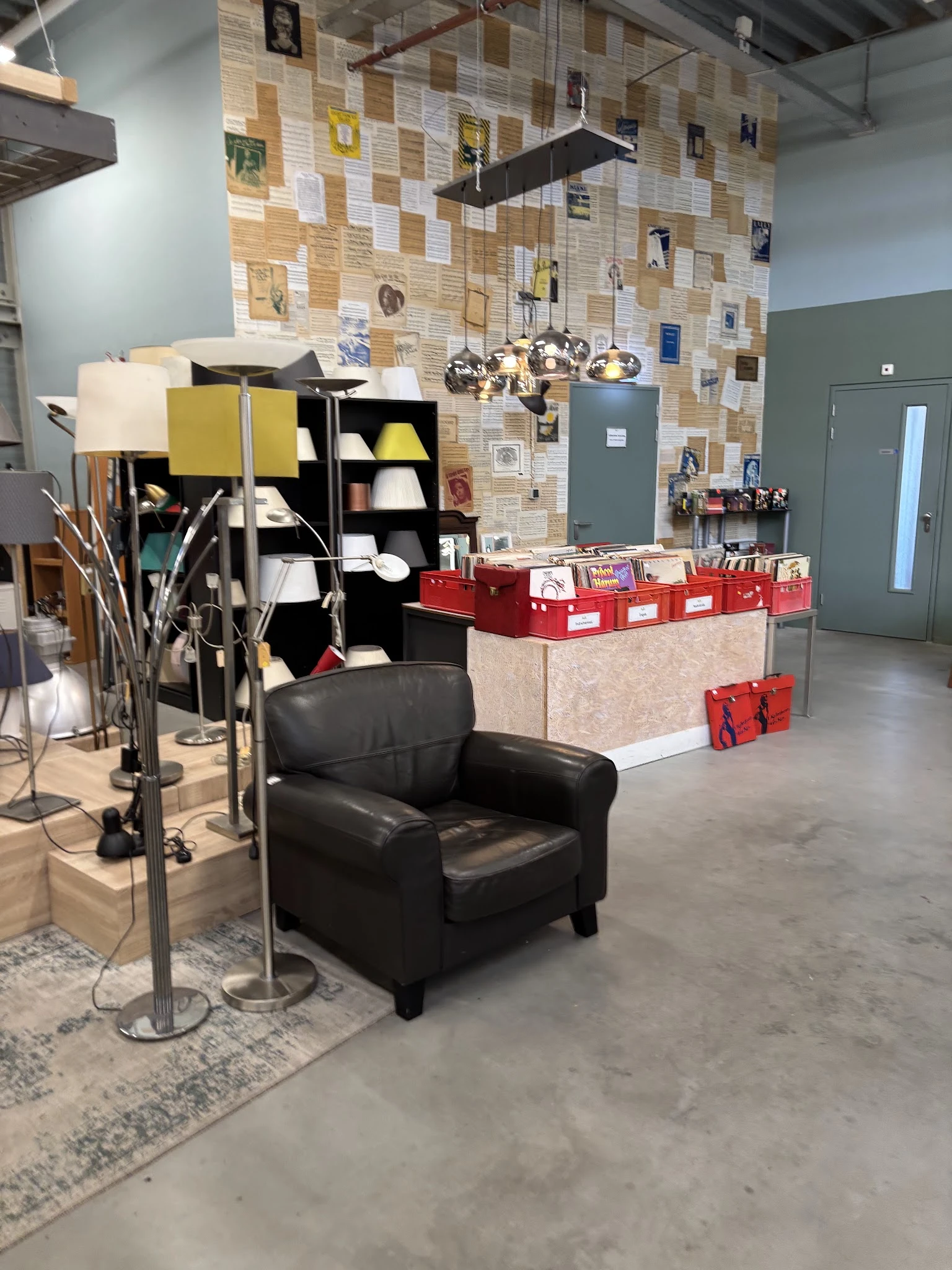Winkelvloer met zwarte fauteuil, stellingen met spullen, rode dozen en prikbord met foto's