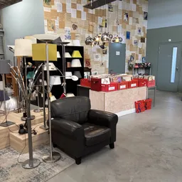 Winkelvloer met zwarte fauteuil, stellingen met spullen, rode dozen en prikbord met foto's
