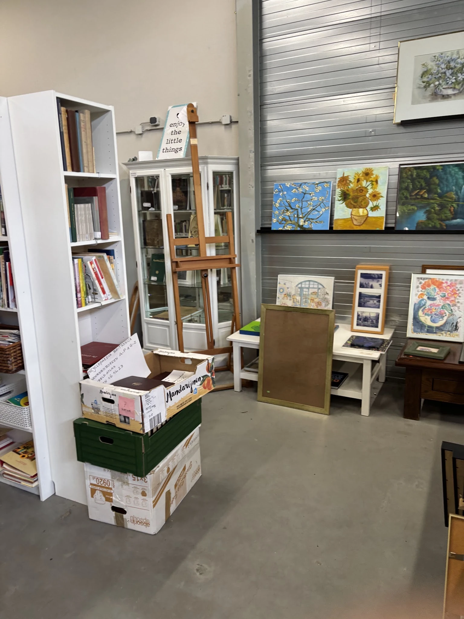 Winkelvloer met boekenkasten, stellingen met kunstwerken aan de muur en diverse tweedehands spullen op display