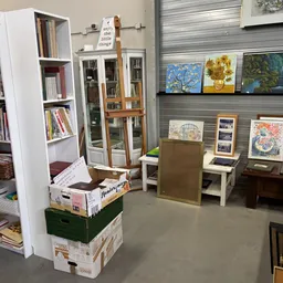 Winkelvloer met boekenkasten, stellingen met kunstwerken aan de muur en diverse tweedehands spullen op display