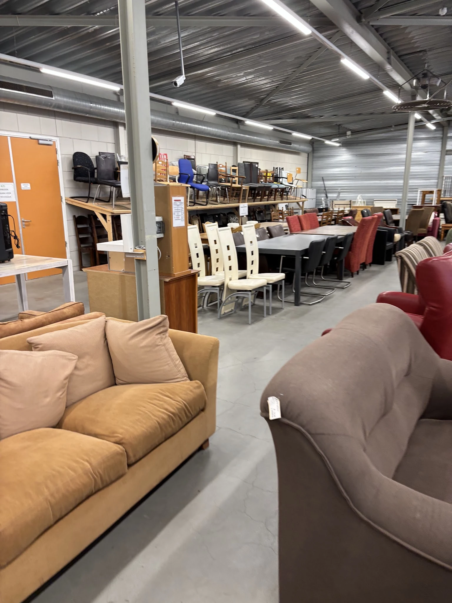 Winkelvloer met meubels: beige fauteuil vooraan, zwarte tafel met witte stoelen, rode/bordeaux stoelen en banken op de achter