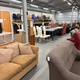 Winkelvloer met meubels: beige fauteuil vooraan, zwarte tafel met witte stoelen, rode/bordeaux stoelen en banken op de achter