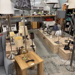 Winkelvloer van kringloopwinkel met houten werktafels, lampen, bureaustoelen en diverse spullen, goed verlicht interieur
