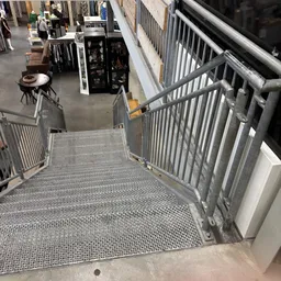Metalen trap en leuningen in een kringloopwinkel met stellingen en spullen zichtbaar op de achtergrond