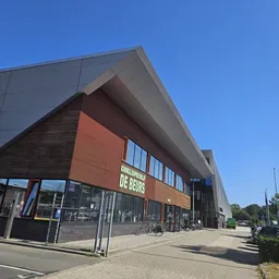 Moderne gevel van kringloopwinkel De Beurs met rode bakstenen en grijze dakconstructie, grote ramen en zichtbare winkelname.
