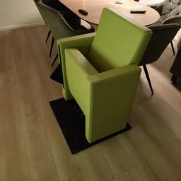 Groene stoel met zwarte poten, staand op houten winkelploer