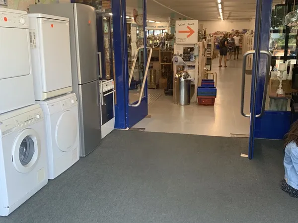 Winkelinterieur met witgoedafdeling, wasmachines en droogkasten links, gang met blauwe zuilen recht vooruit