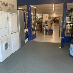 Winkelinterieur met witgoedafdeling, wasmachines en droogkasten links, gang met blauwe zuilen recht vooruit