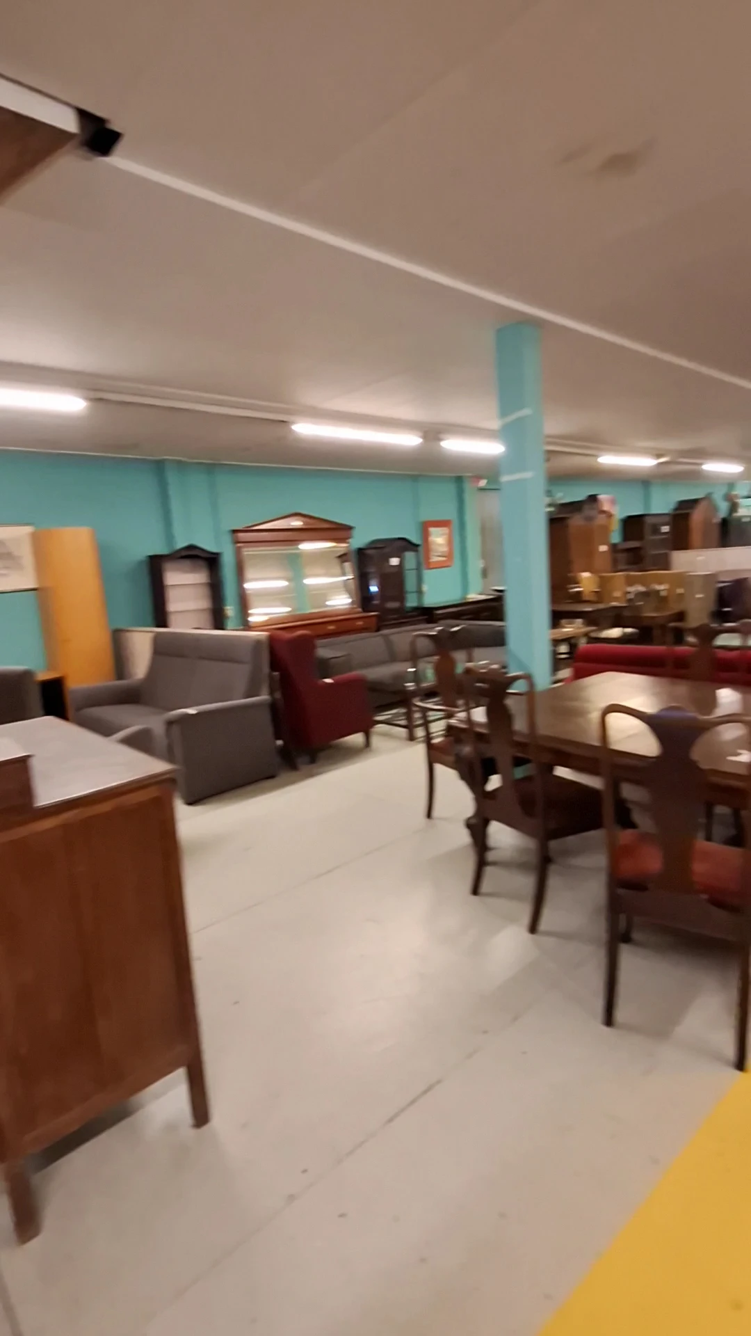 Winkelvloer met meubelstukken: fauteuils, stoelen, tafels en kasten in een ruimte met turquoise wand en halogeenverlichting