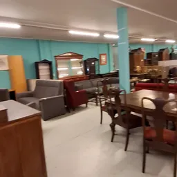 Winkelvloer met meubelstukken: fauteuils, stoelen, tafels en kasten in een ruimte met turquoise wand en halogeenverlichting