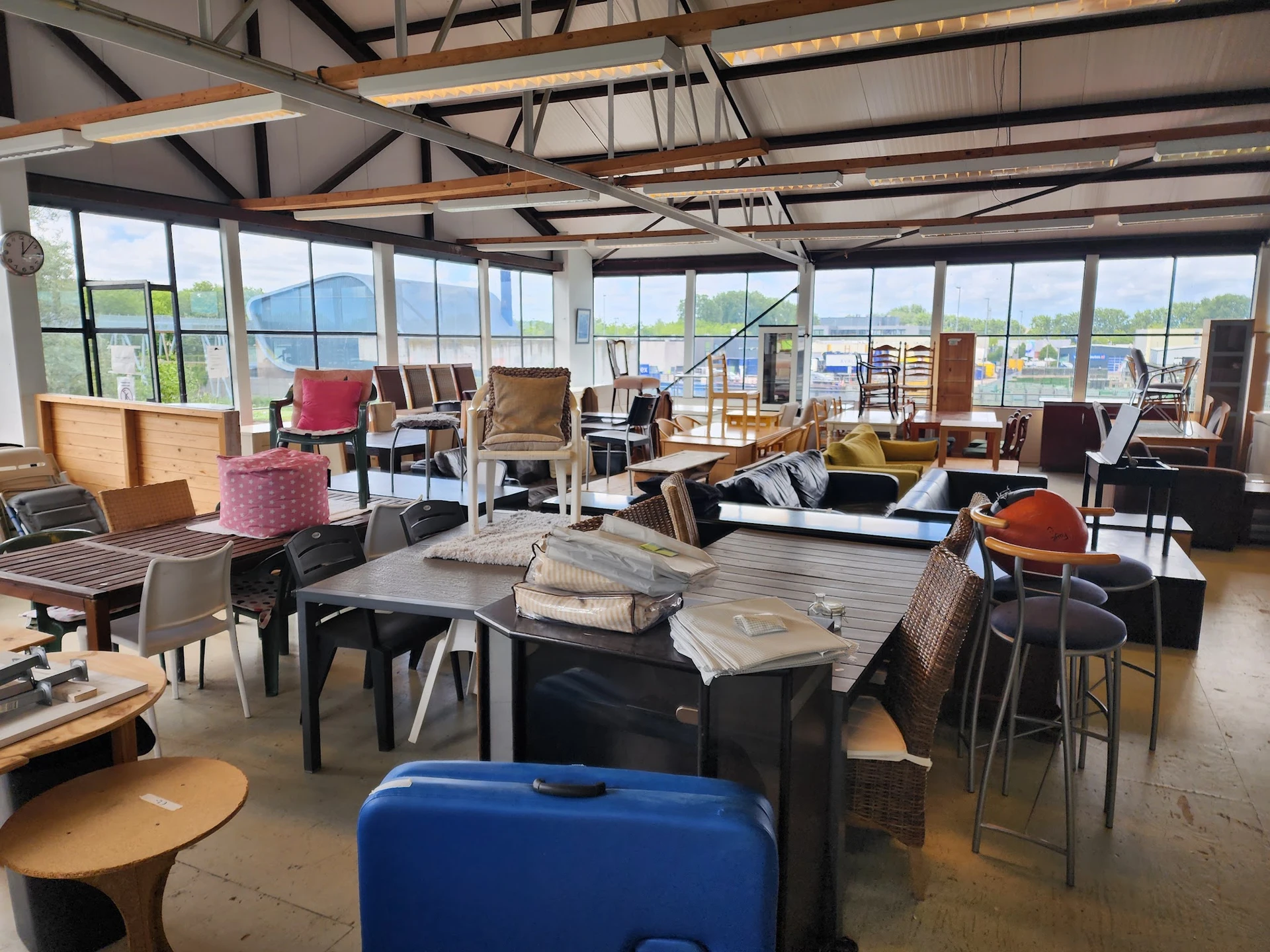 Ruime winkelruimte met diverse tweedehands meubels, stoelen, tafels en huishoudartikelen, grote ramen met uitzicht