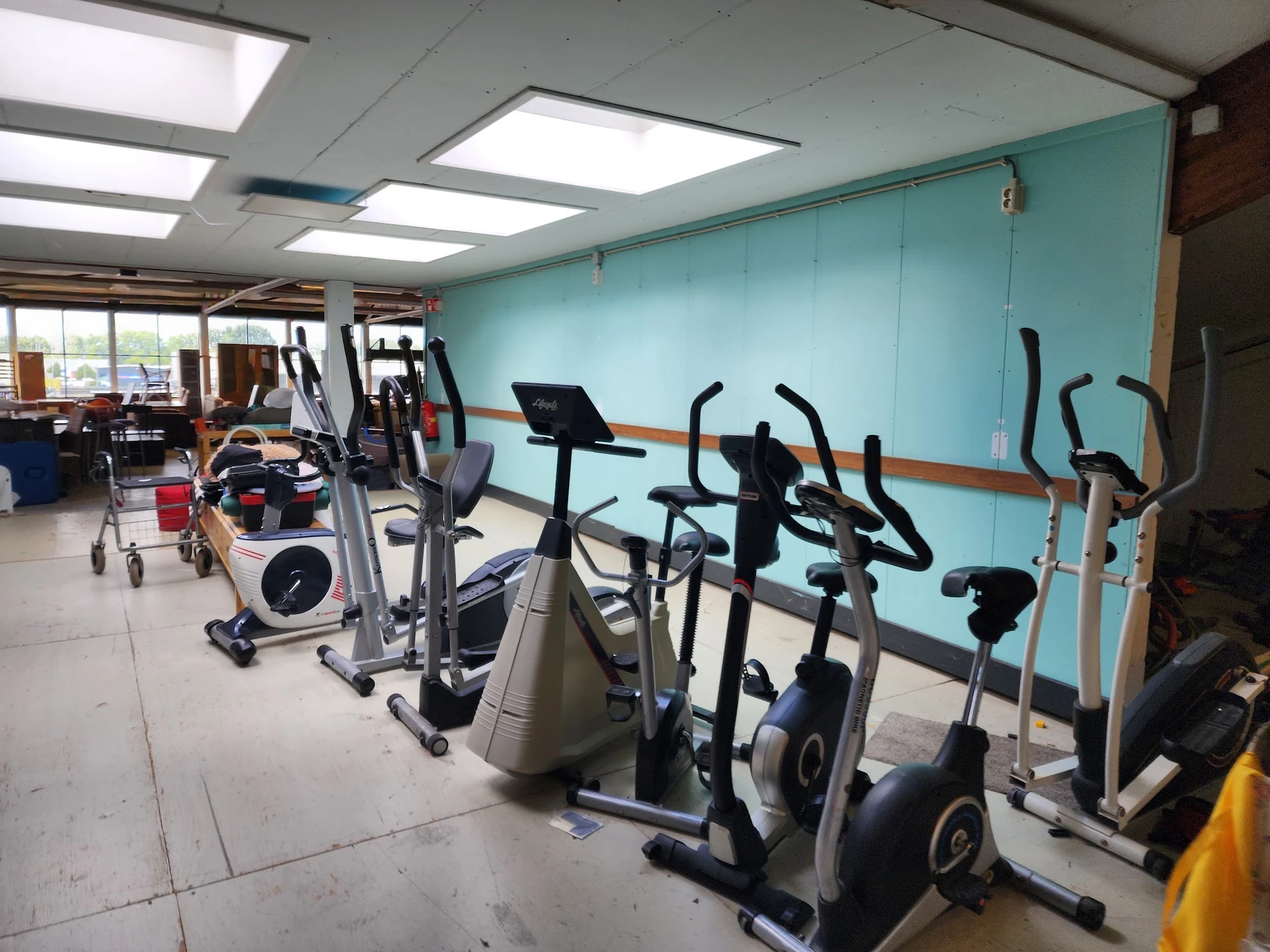 Fitnessapparaten zoals hometrainers en crosstrainers in een kringloopwinkel met turquoise wand