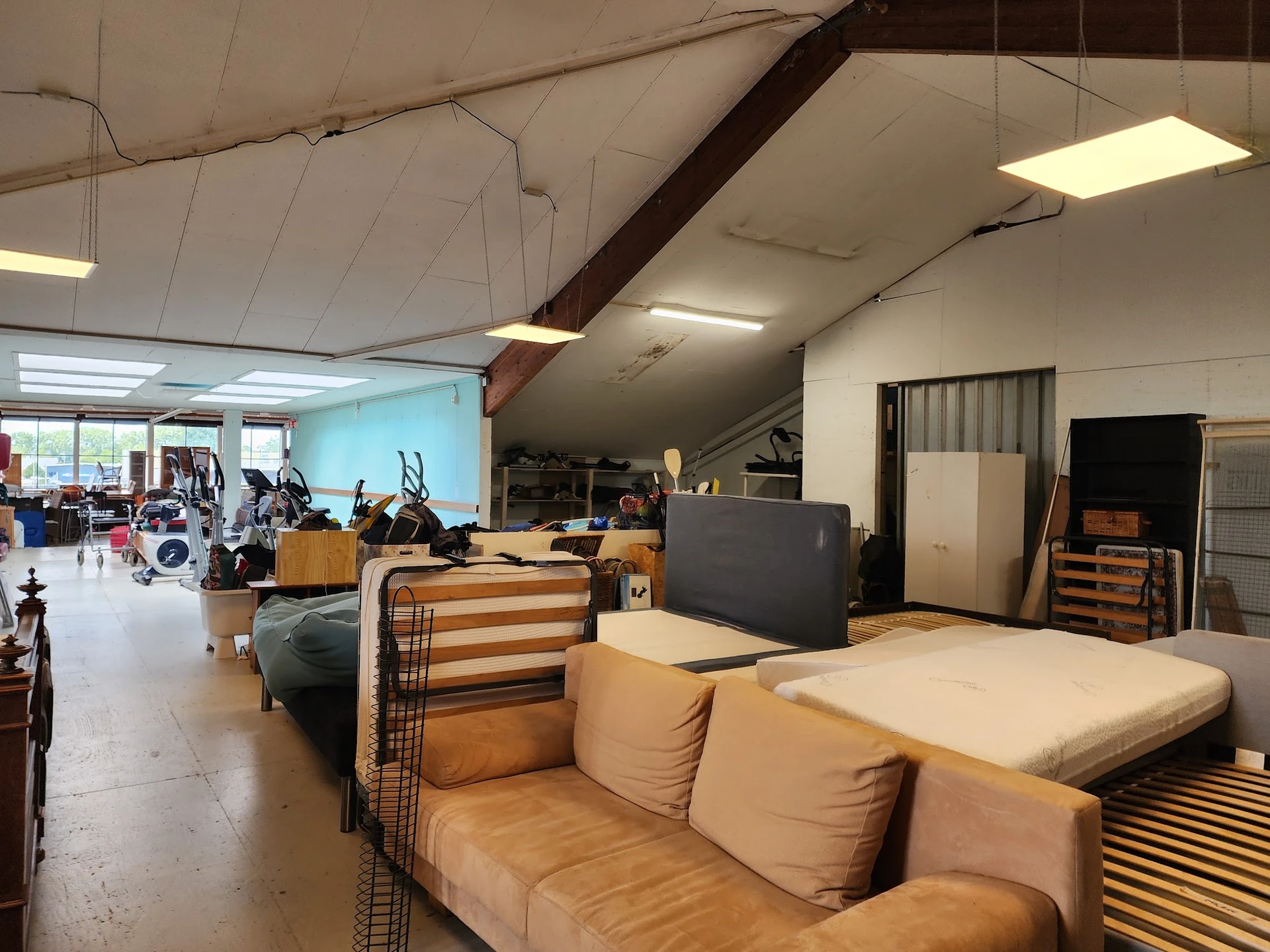 Winkelvloer met bruine stoffeerbank, zwart dressoir en diverse meubels en spullen in een grote hal