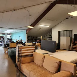 Winkelvloer met bruine stoffeerbank, zwart dressoir en diverse meubels en spullen in een grote hal