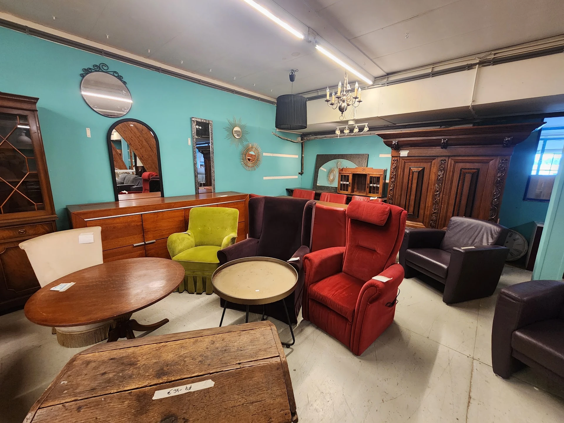 Winkelinterieur met vintage meubels: houten tafels, gekleurde fauteuils, spiegels en kasten tegen turquoise muur