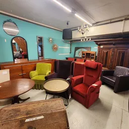 Winkelinterieur met vintage meubels: houten tafels, gekleurde fauteuils, spiegels en kasten tegen turquoise muur