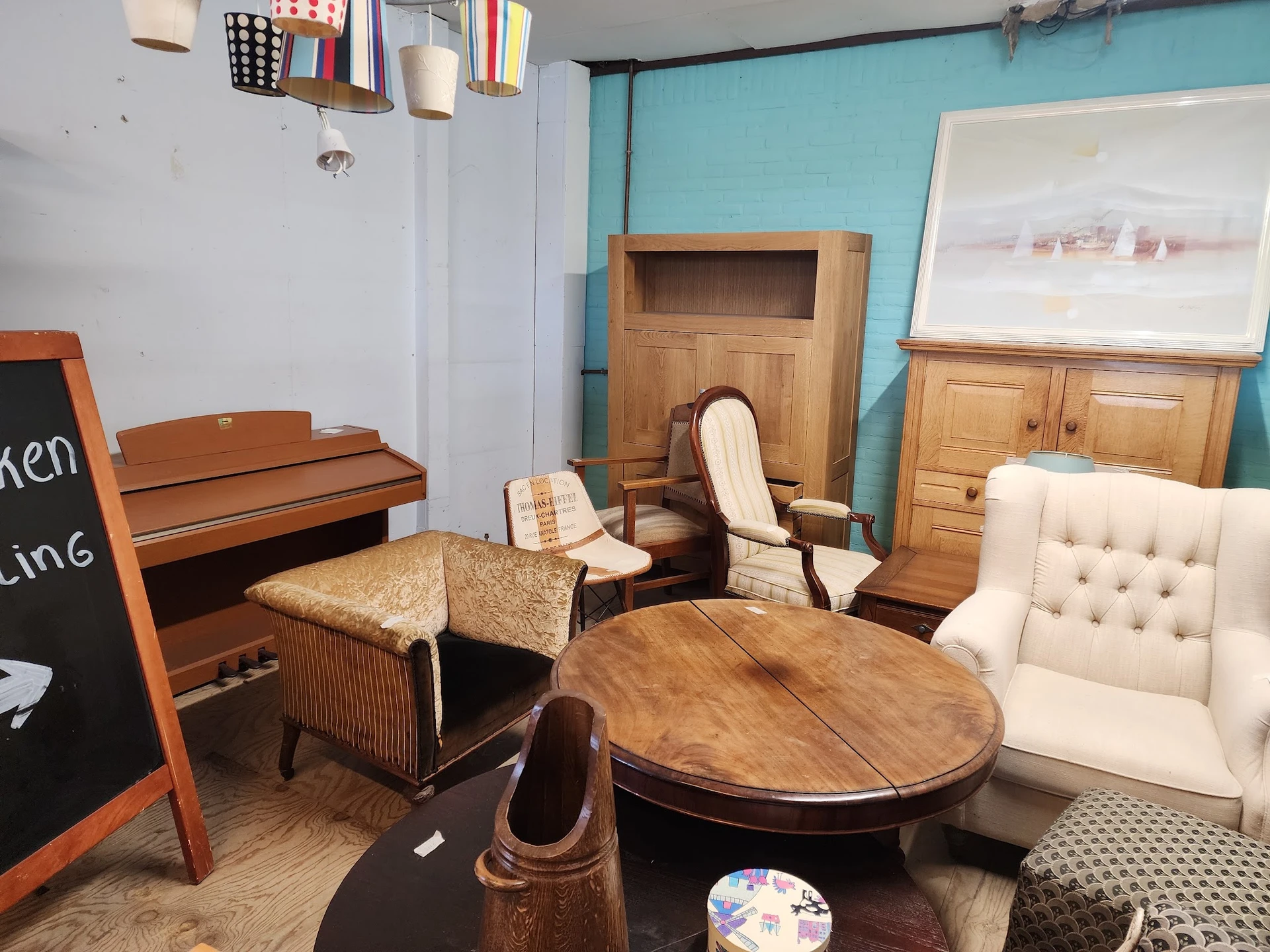 Showroom met tweedehands meubels: houten tafels, stoelen, fauteuils en kasten tegen turquoise en witte wanden