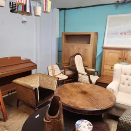 Showroom met tweedehands meubels: houten tafels, stoelen, fauteuils en kasten tegen turquoise en witte wanden