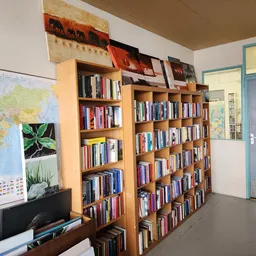 Boekenkasten vol boeken in een kringloopwinkel, met een wereldkaart en plantafbeelding aan de muur
