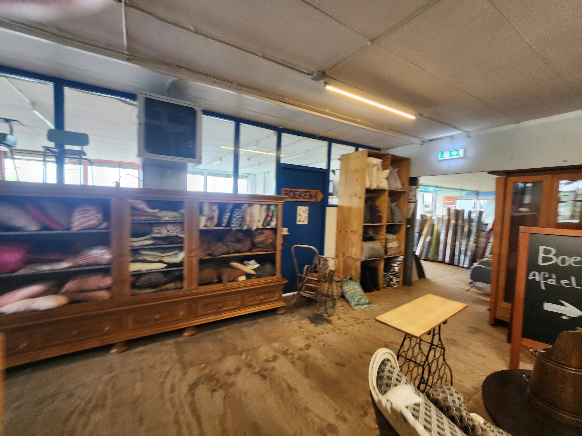 Winkelinterieur met houten kasten, stellingen en diversen spullen, zandvloer zichtbaar