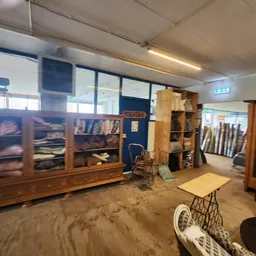 Winkelinterieur met houten kasten, stellingen en diversen spullen, zandvloer zichtbaar