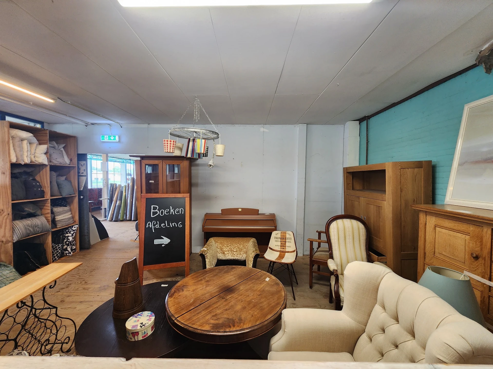 Winkelvloer met houten meubels, fauteuils, kasten en een ronde tafel, turquoise wand op de achtergrond