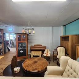 Winkelvloer met houten meubels, fauteuils, kasten en een ronde tafel, turquoise wand op de achtergrond