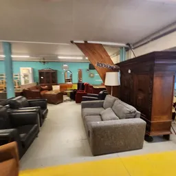 Ruim interieur van kringloopwinkel met meubels, zithoeken, houten boot aan plafond en turquoise wanden