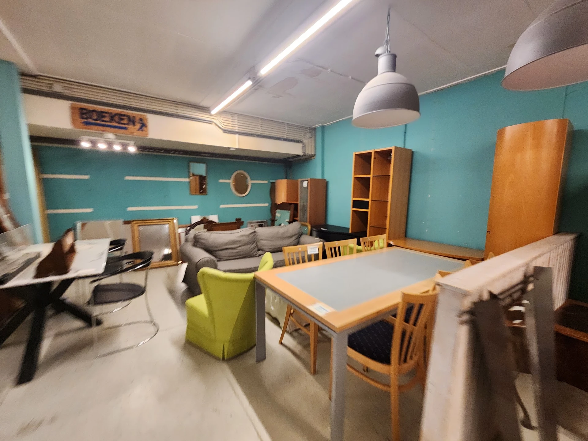 Ruime winkelruimte met turquoise wanden, houten meubels, tafel met stoelen en diverse tweedehands spullen