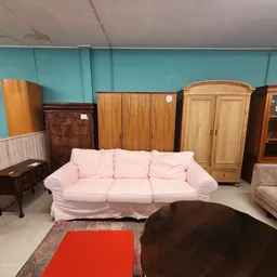 Winkelvloer met tweedehands meubels: roze bank, kasten, ladeblokken en andere meubelstukken tegen turquoise muur