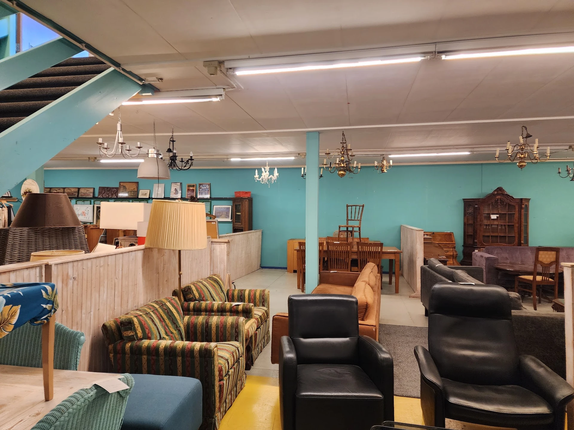 Winkelvloer met tweedehands meubels: fauteuils, stoelen, kasten en lampen tegen turquoise wanden