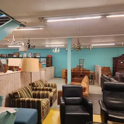 Winkelvloer met tweedehands meubels: fauteuils, stoelen, kasten en lampen tegen turquoise wanden