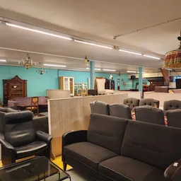 Winkelvloer met zitmeubels: zwarte fauteuils en banken, houten kasten en rekken, turquoise muren, fluorescerende verlichting