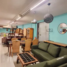 Woonkamer-achtig interieur met groen fluwelen bank, houten eettafel met rotan stoelen, en diverse meubels tegen turquoise mur