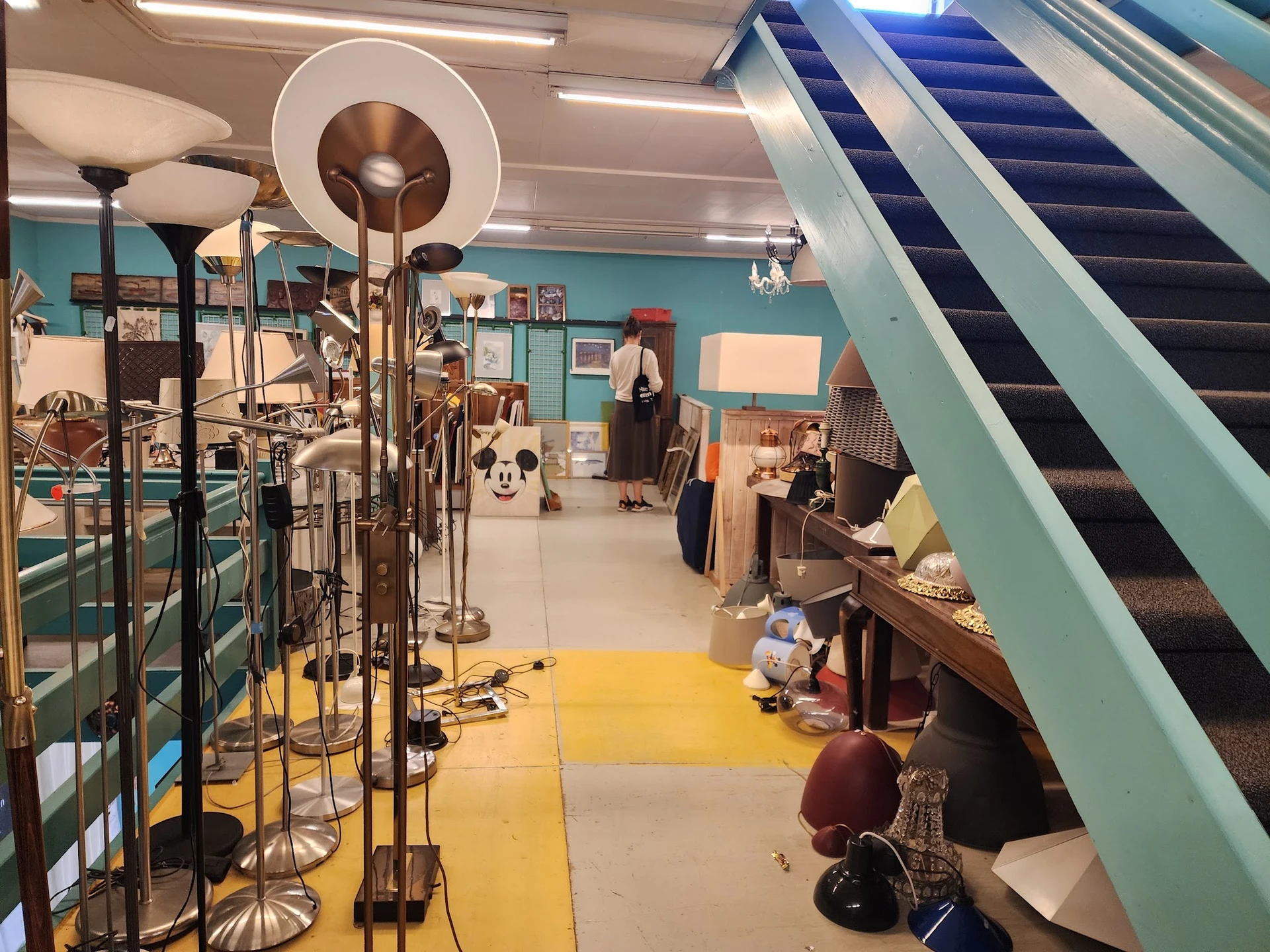 Winkelinterieur met turquoise muren, gele vloer, muziekinstrumenten, meubels en een roltrap