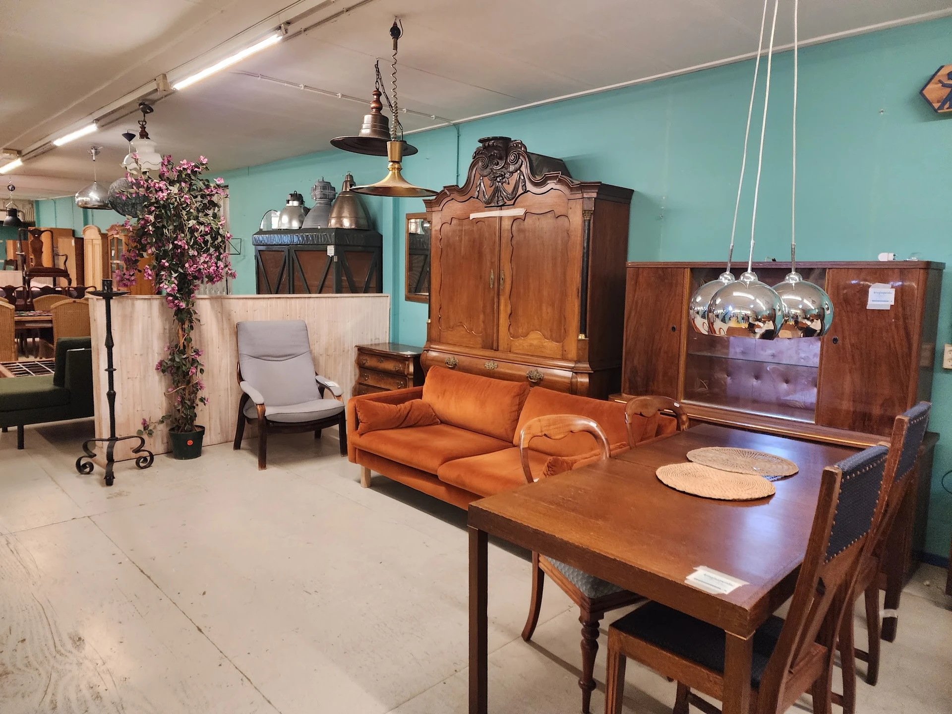 Tweedehands meubels in een kringloopwinkel: houten eettafel met stoelen, oranje bank, kasten en lampen